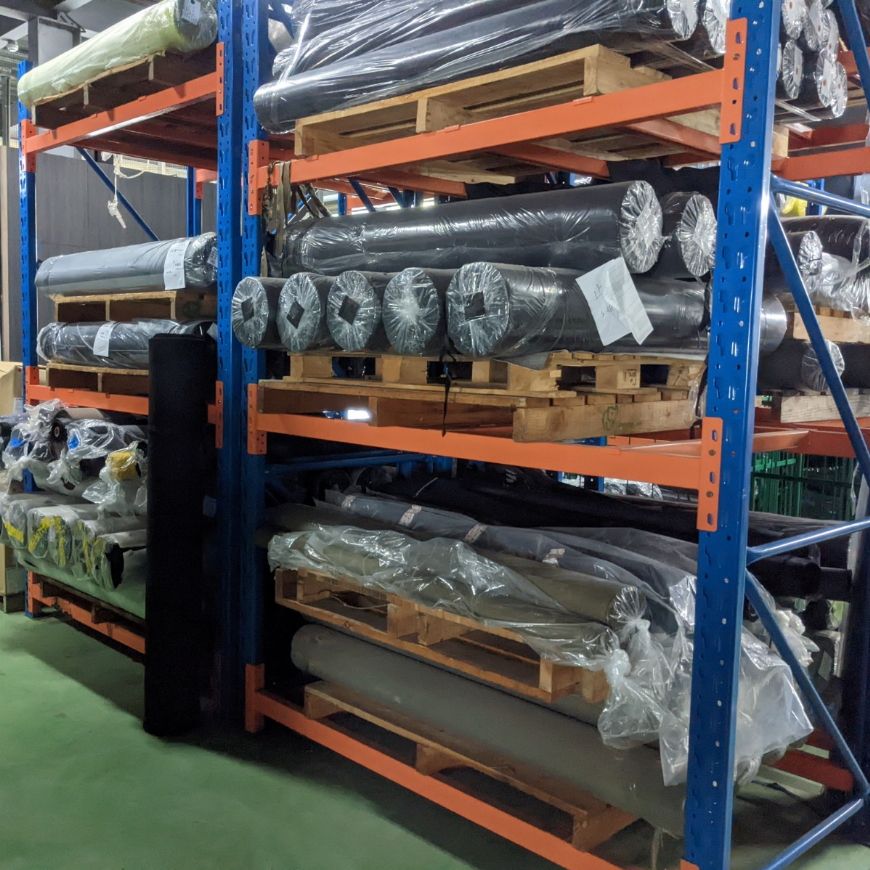 Warehouse storage rack with multiple rolls of packaged fabric, illustrating available material types for tactical bag OEM manufacturing